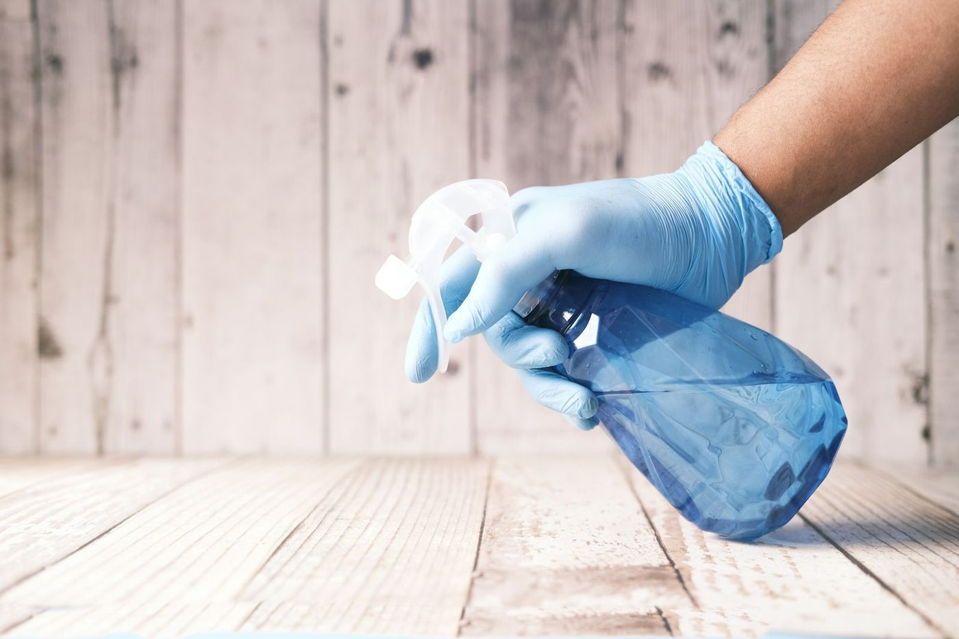 Gloved hand spraying cleaner on a wood surface