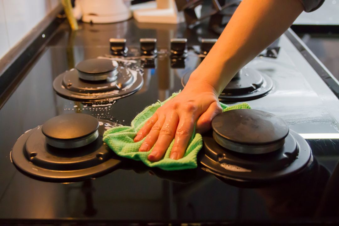 Hand wiping down a gas stovetop with a microfiber cloth