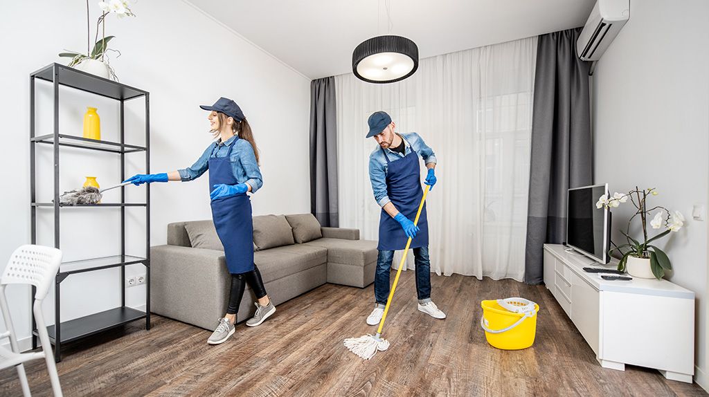 Two cleaners dusting and mopping an empty apartment before move-in